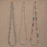 Three Endless Summer Necklaces (Blue Lagoon, Saint-Tropez and Capri) on a beige fabric background. 