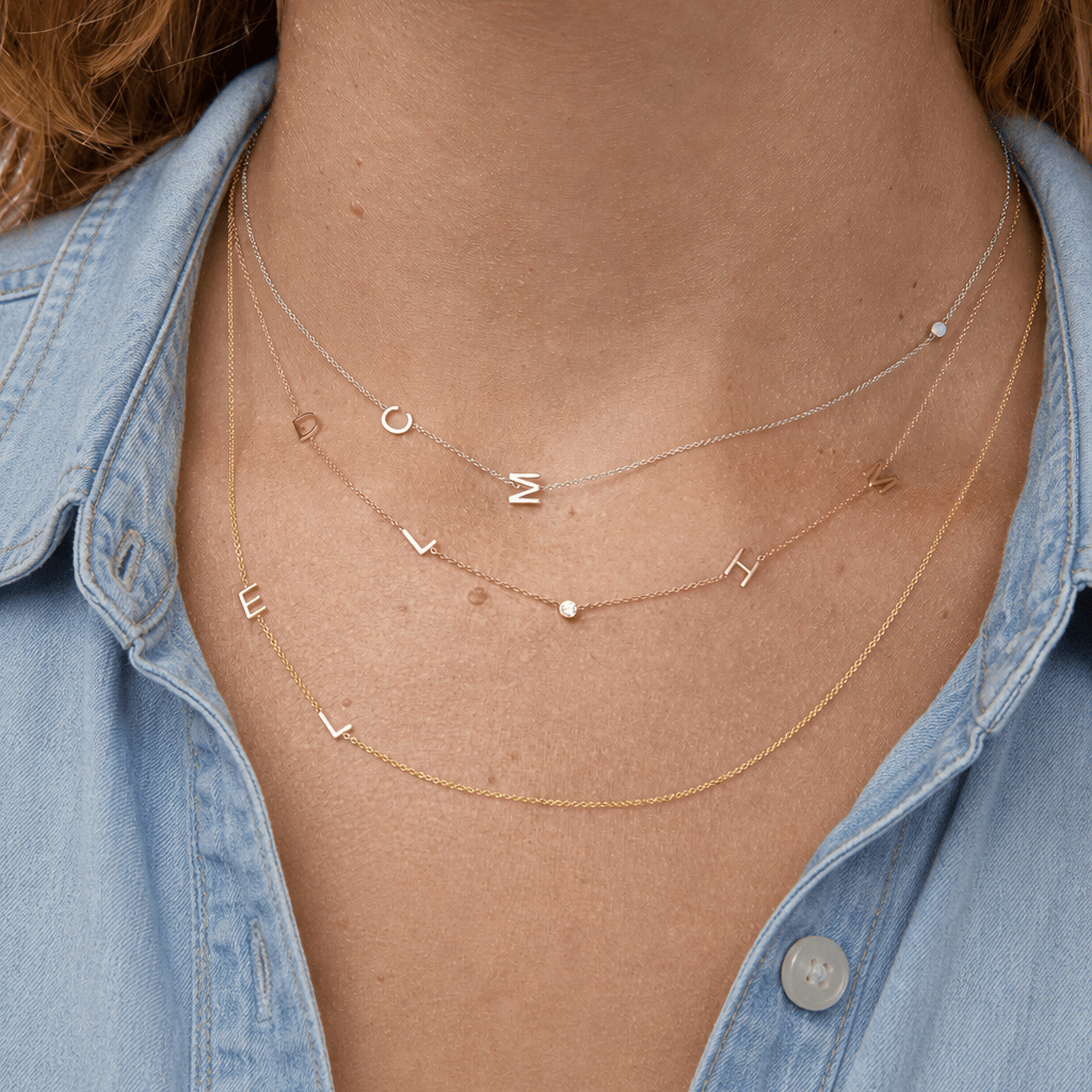 Necklace with letter pendants worn by a person wearing a denim shirt.