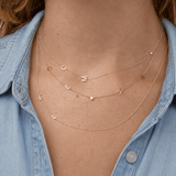 Necklace with letter pendants worn by a person wearing a denim shirt.