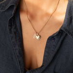 14k gold MUM word plate charm necklace styled with heart locket pendant on model.