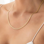 Close-up of a décolletage wearing a Chic Cuban Curb Chain in yellow gold with a white strap top. 