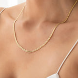 Close-up of a décolletage wearing a Chic Cuban Curb Chain in yellow gold with a white strap top. 