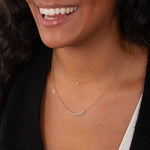 Close-up of a woman's neck wearing a Single Diamond Layering Necklace, a Diamond Arc Layering Necklace and a Custom Gold Necklace - 1 Letter, all in yellow gold, in a black top. 