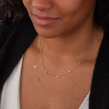 Close-up of a woman's  neck wearing a Quintet Diamond Layering Necklace and a Custom Gold Necklace - 2 Letters with a white top and black cardigan. 