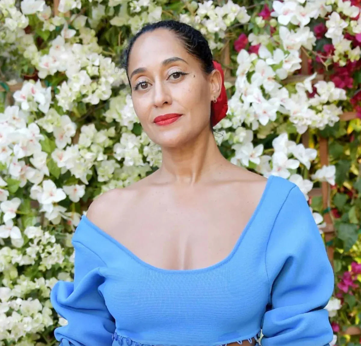A woman wearing an Open Eclipse Earring - Small in yellow gold with a blue top and red lipstick against a floral background. 