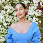 A woman wearing an Open Eclipse Earring - Small in yellow gold with a blue top and red lipstick against a floral background. 