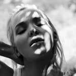 Black and white photo of a woman wearing an Open Eclipse Earring - Small with sunlight casting shadows on her face. 