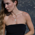 Woman wearing a black strapless top with layered necklaces against a dark background