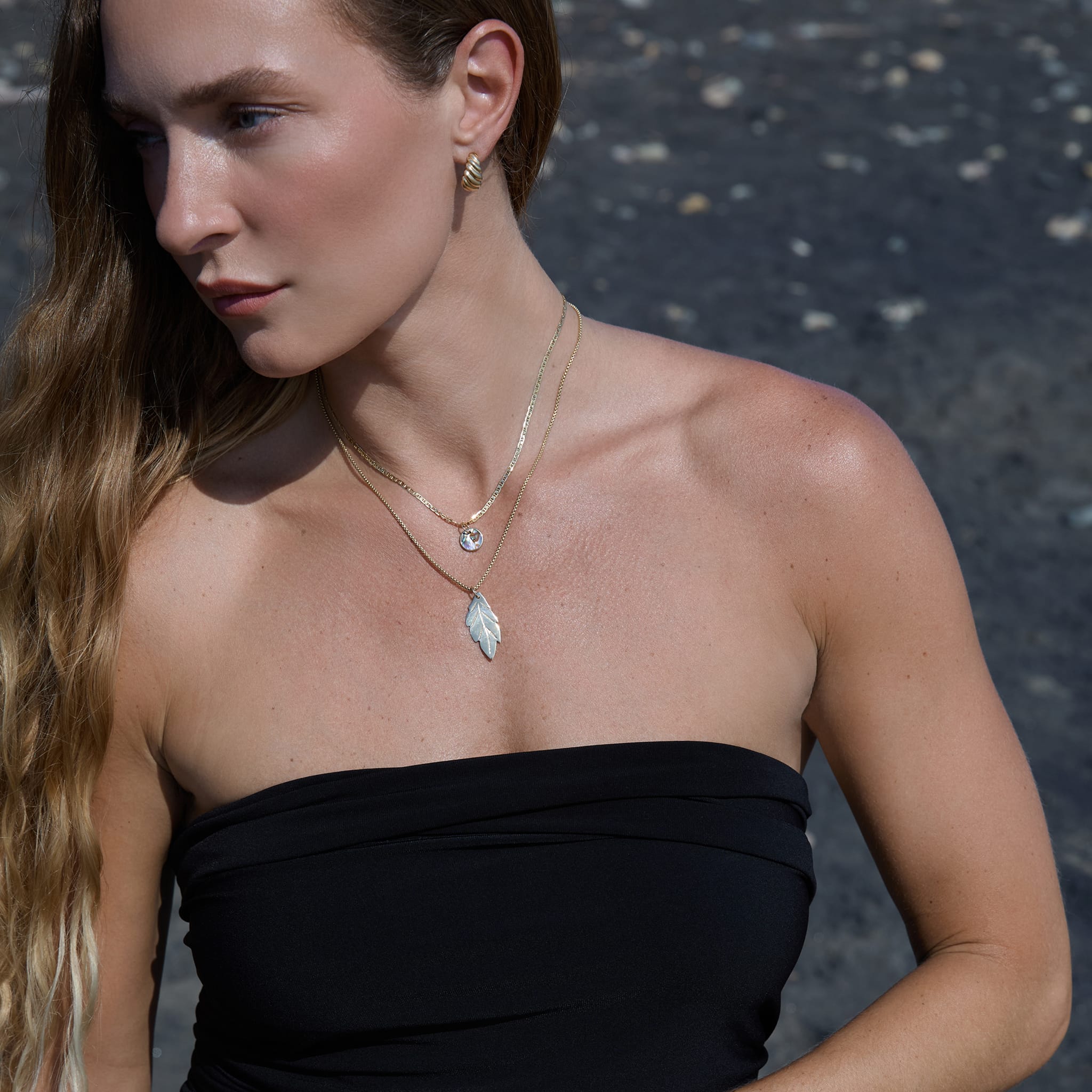 Woman wearing a black strapless top with layered necklaces against a dark background
