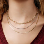 Three gold necklaces in mixed metals on a person wearing a red top.