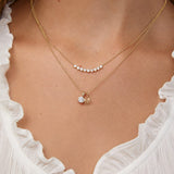 Gold necklace with a letter 'M' and pave cross pendant on a person wearing a white top.