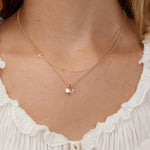 Gold necklace with a letter 'M' and pave cross pendant on a person wearing a white top.
