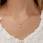 Gold necklace with a letter 'M' pendant on a person wearing a white top.