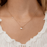 Gold necklace with a letter 'M' pendant on a person wearing a white top.