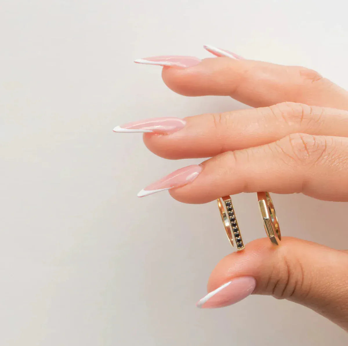 A hand holding a Pave Geo Ring - Black Diamond and Tenfold Ring in yellow gold against a light grey background. 