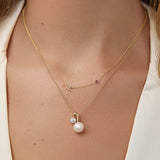 Close-up of a person wearing a gold necklace with a pearl pendant.