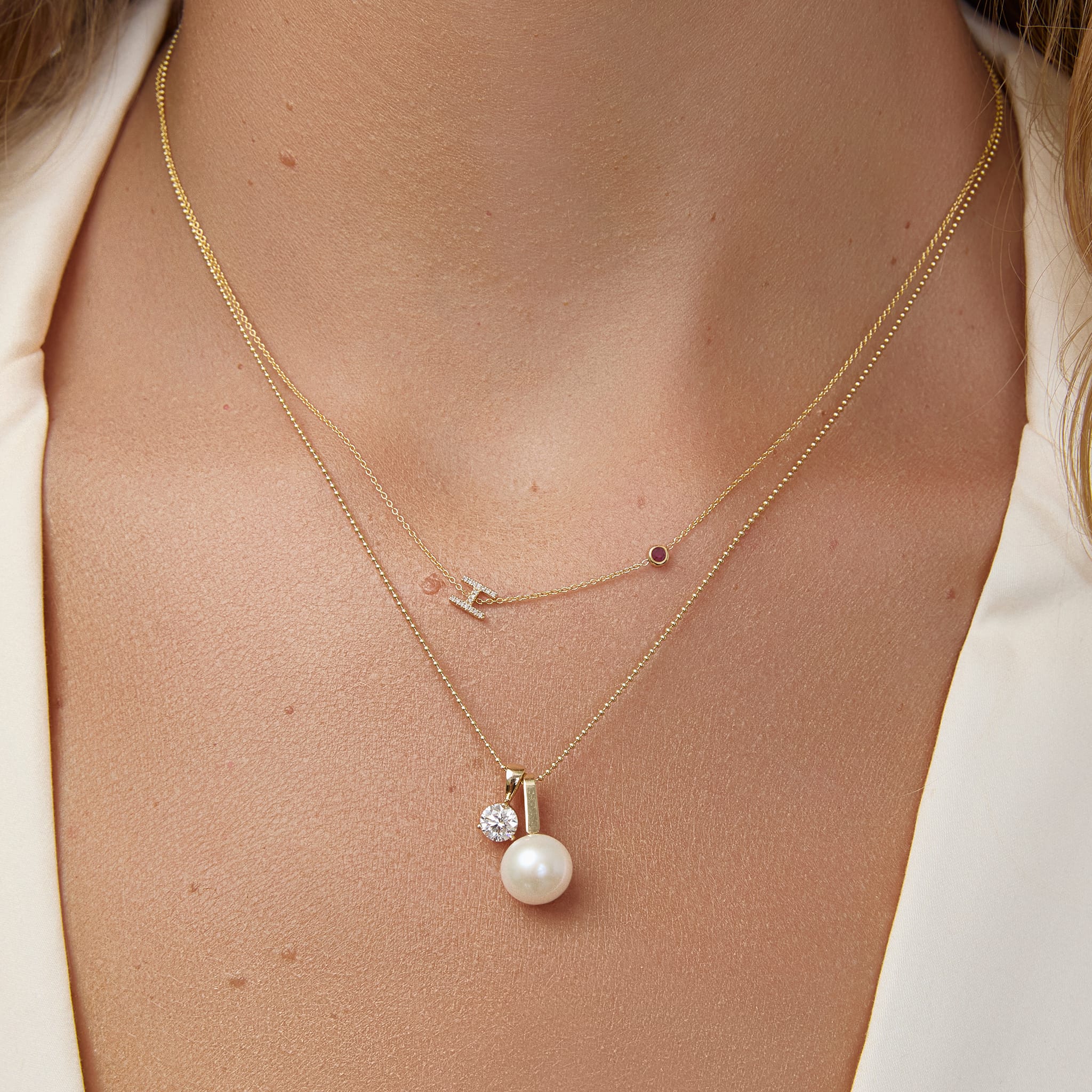 Close-up of a person wearing a gold necklace with a pearl pendant.