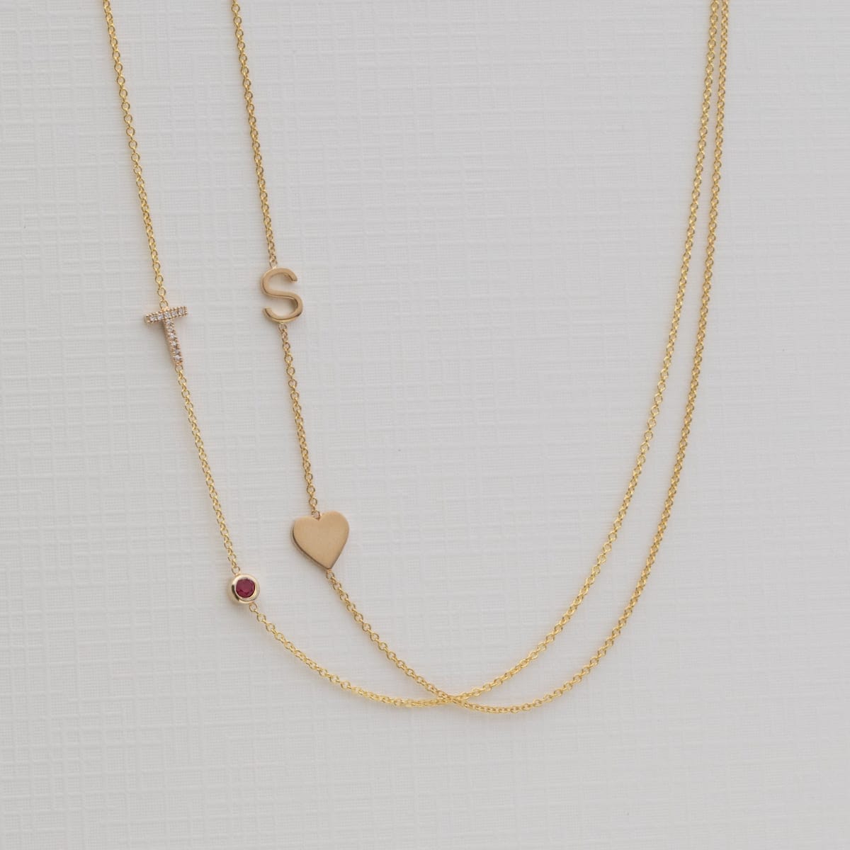 Gold necklace with small heart and letter 'S' pendant on a light gray background