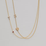 Gold necklace with small heart and letter 'S' pendant on a light gray background