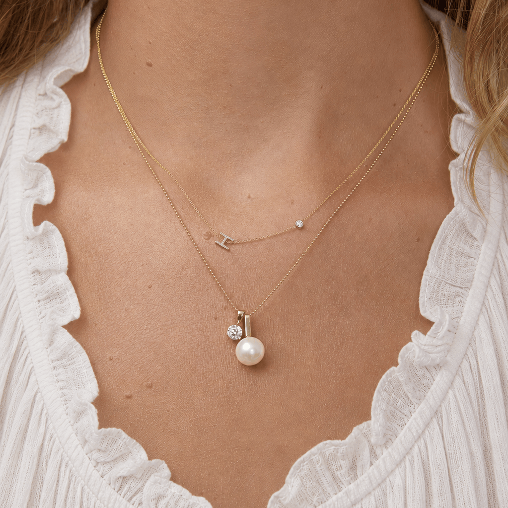 Close-up of a gold necklace with a pearl pendant worn by a person.