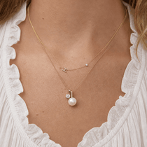 Close-up of a gold necklace with a pearl pendant worn by a person.