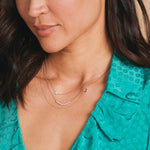 Close-up of a woman wearing a delicate necklace with a green top.