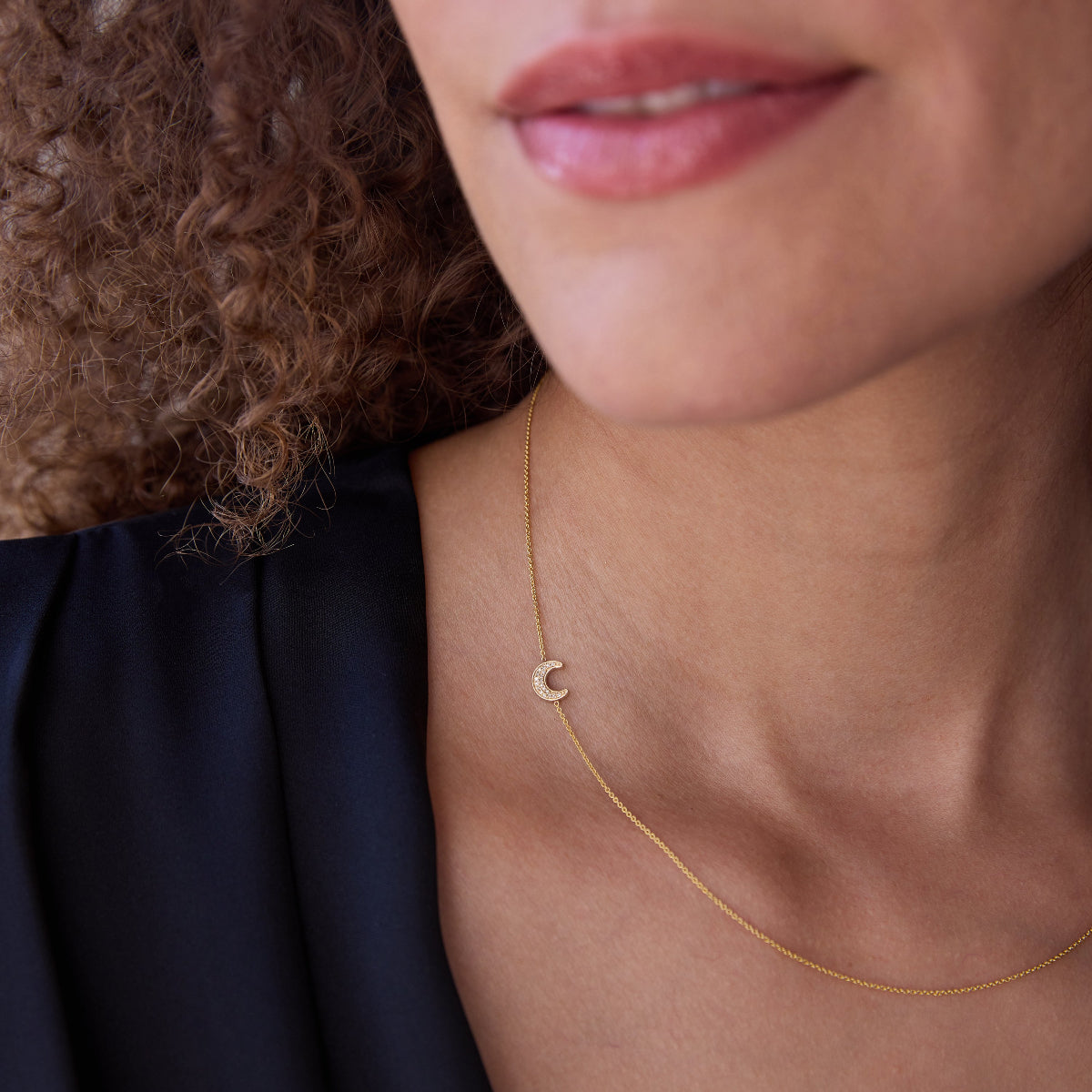 A woman in a blue top wearing a pave moon charm gold necklace.