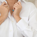 A woman wearing several The Lily Bouquet Necklaces layered in different lengths with an Etched Turquoise Heart Charm, The Lily Bouquet Necklace and a Perla Pinky Ring, styled in a white shirt. 