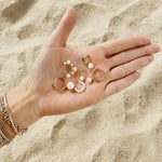 Gold hoop earrings with freshwater pearls held in an open hand against sandy beach background — pearl earring charms, pearl hoop earrings, and gold huggie hoops by Maya Brenner