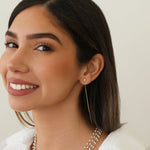 A woman wearing a Pearl Drift Threader, several The Lily Bouquet Necklaces and a white top, with brown hair against a neutral background.