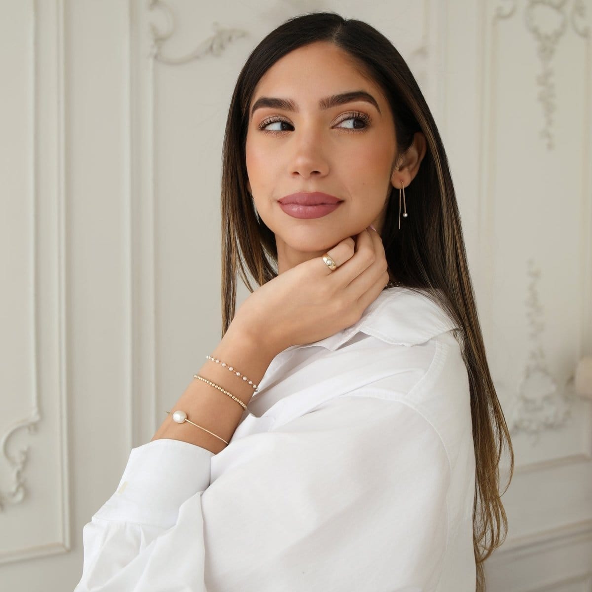 A woman wearing The Lily Bouquet Bracelet, Baroque White Pearl Bangle, Little Bubble Bracelet, Perla Pinky Ring and Pearl Drift Threader, styled with a white shirt. 