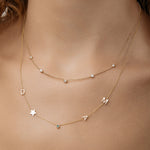Gold necklace with letter charms on a person's neck layered with a necklace that has five diamonds on it.