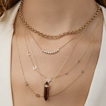 Layered gold necklaces with various pendants on a neck.