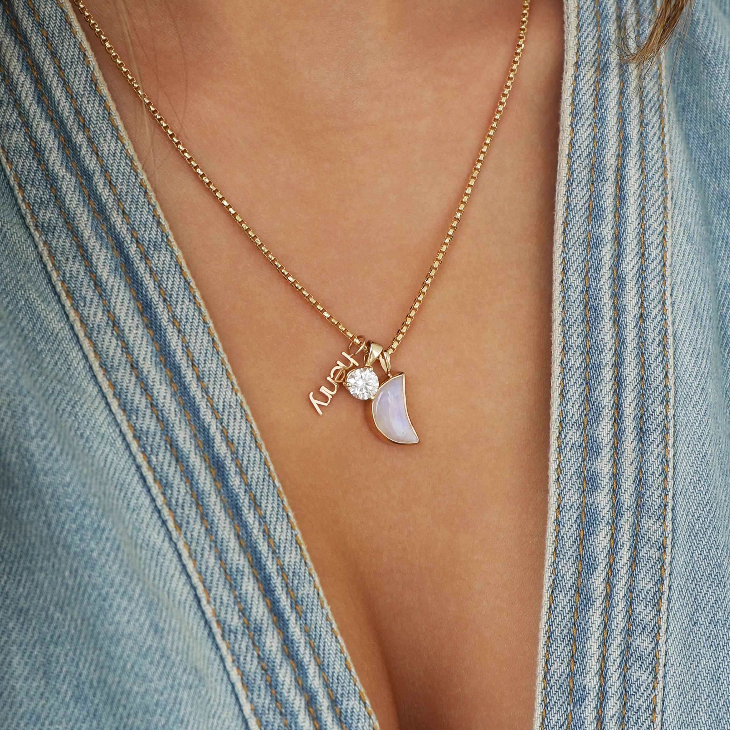 moon charm, diamond charm, vertical name necklace together on a gold box chain.