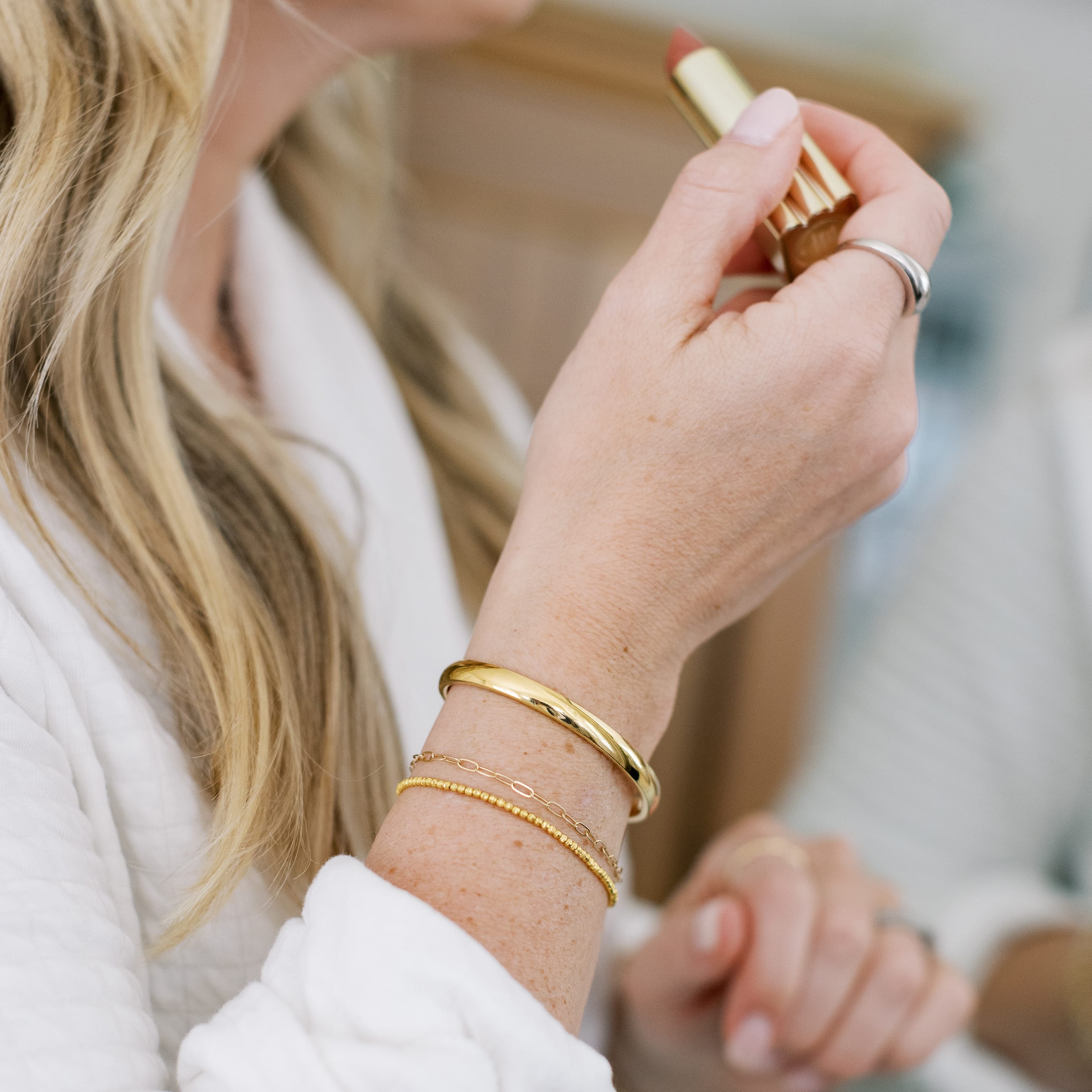 Person applying lipstick with a focus on hands and jewelry