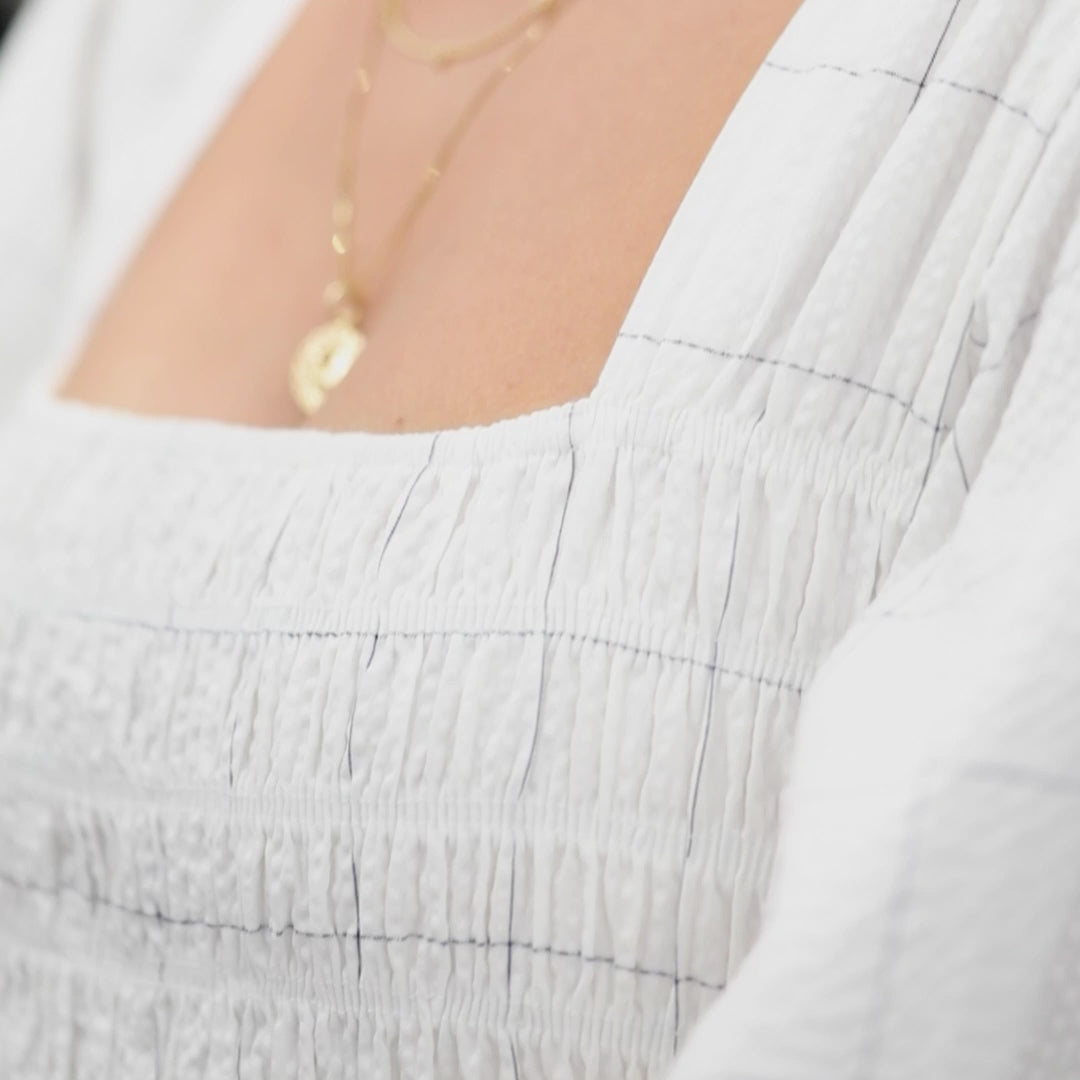 A video of a woman wearing an Overboard Layering Chain, an Element Short Link Chain, A Quintet Birthstone Layering Necklace - Yellow Gold and a Zodiac Necklace - Leo, styled in a white top. 