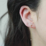 Close-up of a woman's ear wearing a Droplet Diamond Earring and putting on a Coupling Ear Cuff + Stud in yellow gold. 