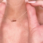 A close-up of a person's neck hold a Petite Nameplate Necklace in rose gold with 'clare'. 