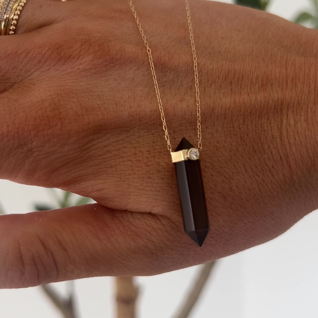 A video of the Courage Retreat Necklace held in front of a hand, with a plant in the background.