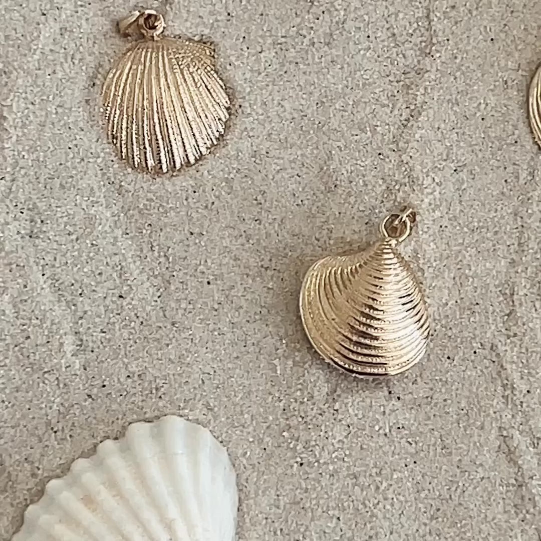 A Golden Scallop Shell, Golden Coast Shell, Golden Venus Shell and a Golden Spiral Shell on an Element Long Link Chain against a sandy background with shells. 