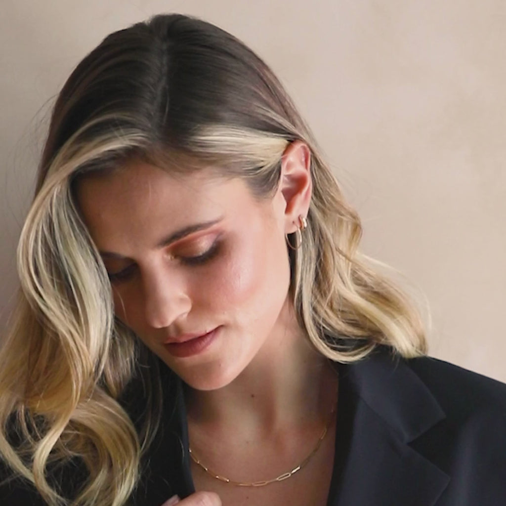 A blonde woman wearing a yellow gold Element Long Link Chain with a black blazer against a light neutral background. 