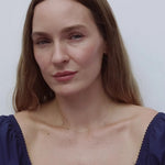 movie of a woman wearing blue top and 3 letter necklace on a white background