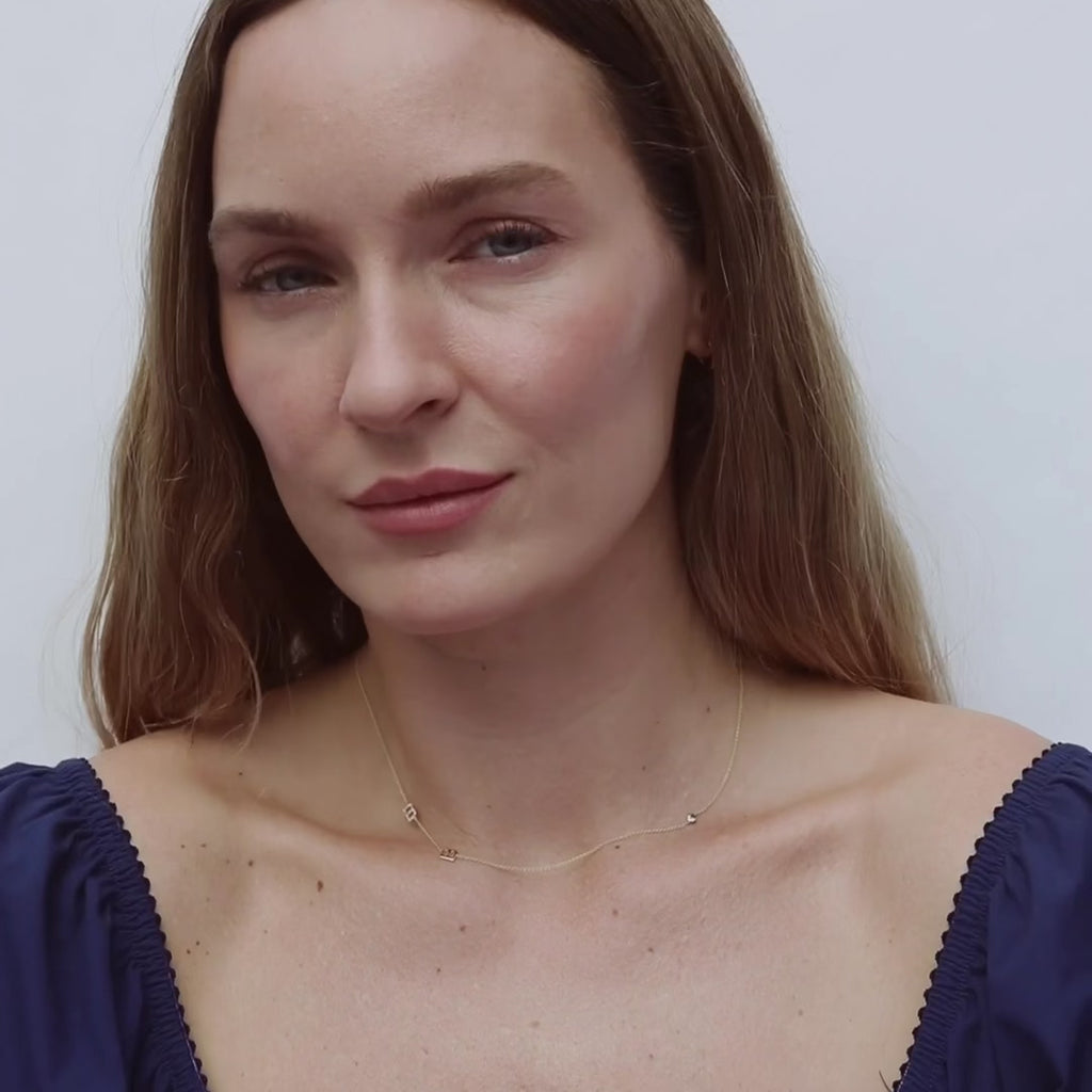 movie of a woman wearing blue top and 3 letter necklace on a white background