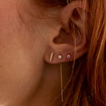 A video of woman's ear wearing a yellow gold Threader Earring Diamond, a Birthstone Stud and a Diamond Bar Earring, with her orange hair visible. 