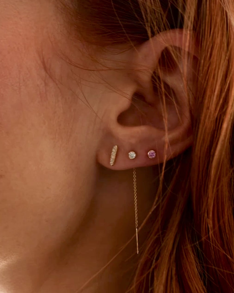 A video of woman's ear wearing a yellow gold Threader Earring Diamond, a Birthstone Stud and a Diamond Bar Earring, with her orange hair visible. 