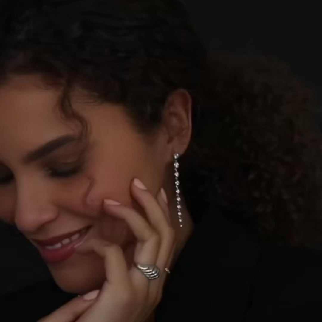 A close-up of a woman wearing a Diamond Cascade Earring and Etched Paris Ring in white gold, with dark brown curly hair. 