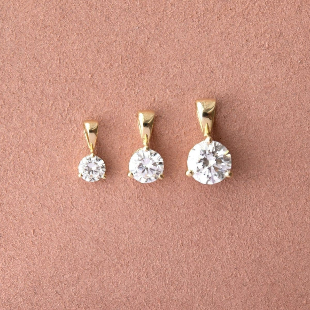 A Duchess Diamond Pendant, Princess Diamond Pendant and Queen Diamond Pendant against a dusty rose color. 