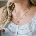Close-up of a person wearing multiple gold necklaces with small pendants.
