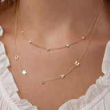 Gold necklace with letter charms on a person wearing a white lace top.
