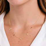 Gold necklace with rainblow , horseshoe, clover, and ribbin charms  on a person wearing a white shirt.